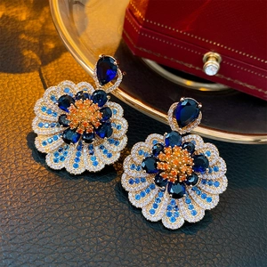 Detailed close-up of luxury flower earrings with deep blue gemstones on red velvet