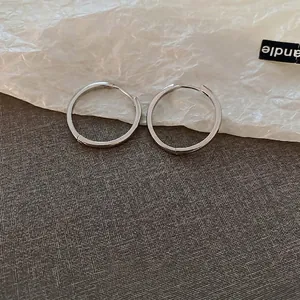 Minimalist silver circular hoop earrings displayed on a clean textured aesthetic background