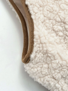 Close-up of fluffy cream faux fur fabric with brown piping detail on the vest