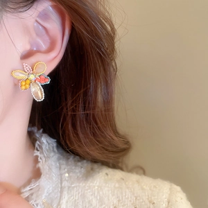 Macro shot of a beaded floral earring in orange and yellow on a model's ear