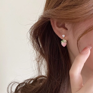 Close-up of pink strawberry earrings with heart rhinestones worn by a model