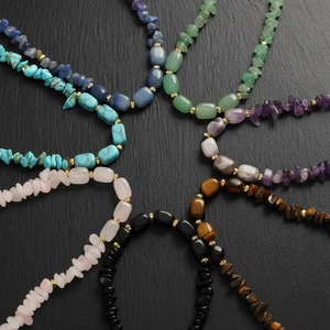 Macro shot of assorted natural stone necklaces with gold beads on a dark rock background