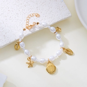 Detail of bohemian pearl bracelet with gold starfish and shell pendants on textured stone