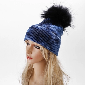 Detail of blue tie-dye knit beanie with large black faux fur pom pom and ribbed texture