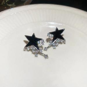 Close-up of star drop earrings with black enamel and sparkling rhinestones on white plate