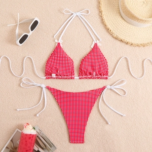 Flat lay of red gingham bikini set with straw hat and sunglasses on beach sand