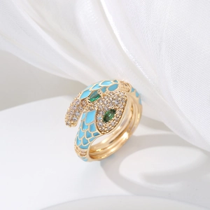 Macro shot of gold snake ring with light blue enamel scales and green gemstone eyes