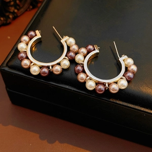 Détail de boucles d'oreilles dorées en C avec perles multicolores sur écrin en cuir noir