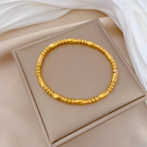 Detail of a minimalist gold beaded stainless steel bracelet on white silk in a jewelry box