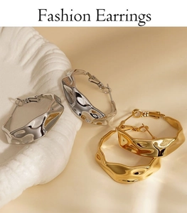 Detail of irregular pleated C-shape earrings in gold and silver finish on beige background