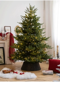 Detail of warm-lit Christmas tree with lush branches and a rustic woven basket tree stand