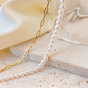 Elegant gold paperclip chain and white pearl necklace on natural stone display