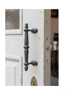 Detail of vintage black iron door handle with cast texture on distressed white wooden door