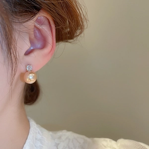Detail view of champagne pearl earrings with round zircon studs on a female model