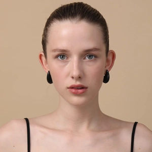 Close-up of black teardrop enamel earrings worn by a model in a minimalist style