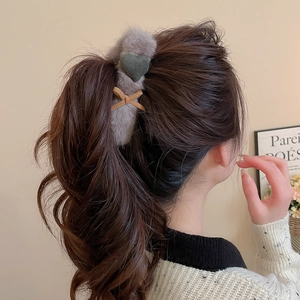 Detail view of grey plush hair claw with green heart and bow on wavy brown hair