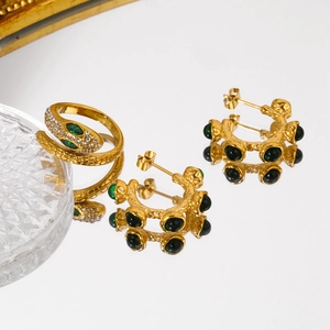Detail of 18k gold plated snake ring and green gemstone earrings set on a mirror