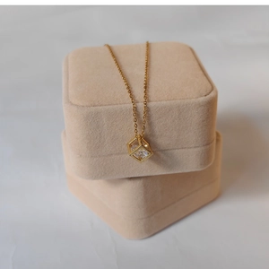 Gold necklace with geometric cube pendant draped over soft beige velvet jewelry boxes