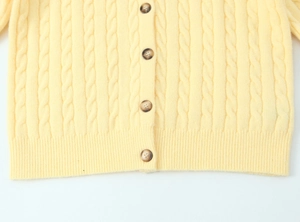 Detail of pale yellow cable-knit cardigan showing textured weave and tortoise buttons
