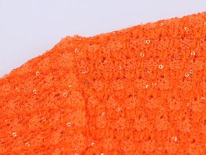 Detailaufnahme von orangefarbenem Strickstoff mit glänzenden silbernen Pailletten