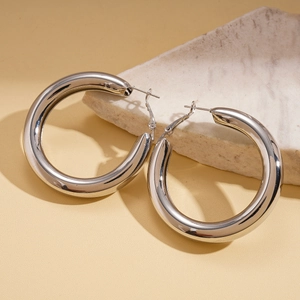 Close-up of chunky silver metallic hoop earrings with polished mirror finish on marble stone