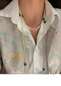 Detail of a multi-layer faux pearl necklace featuring green beads and golden accents