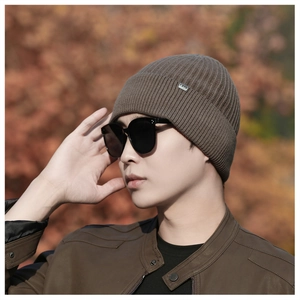 Outdoor close-up of a brown ribbed knit beanie with a square brand patch on the cuff