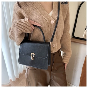 Detail of a black PU leather handbag with a gold metal clasp and adjustable shoulder strap