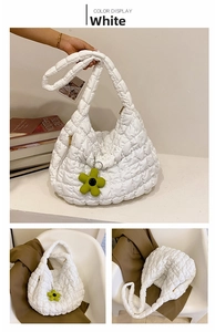 Macro detail of white quilted puffer tote bag with green floral charm and soft fabric texture