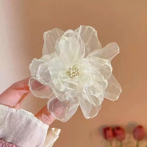 Close-up of a white transparent organza flower hair clip held against a pink background