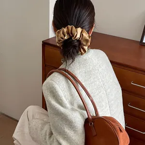 Detail of a large champagne silk scrunchie styled on a model's hair in a retro setting