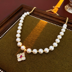 Detailed shot of white pearls, red gemstone and gold clover pendant on luxury necklace