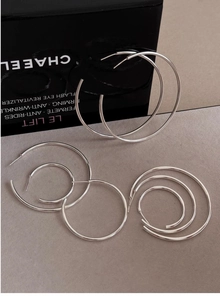 Three pairs of silver hoop earrings in varying sizes displayed on a grey background