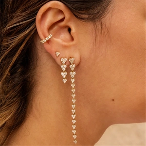 Close-up of gold tassel earrings with heart gems and crystal studs worn by a model