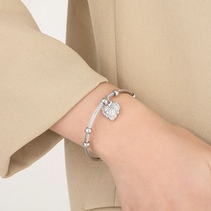 Detail of silver twisted cable cuff bracelet with heart charm on a model wrist