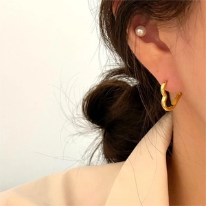 Detailed view of minimalist gold heart hoop earring and pearl stud on a model
