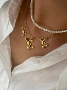 Detail of layered gold crab pendant necklace and white pearl choker on female neck
