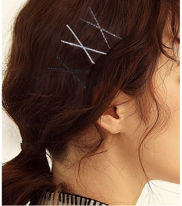 Detail of glitter silver bobby pins worn in a cross pattern on wavy brown hair
