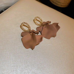 Detail of gold circular studs with brown matte petal pendants on textured surface