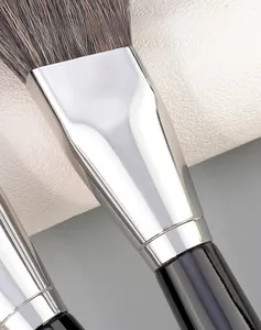 Vue macro de la virole en aluminium argenté et du manche en bois noir du pinceau de maquillage