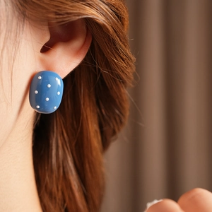 Primo piano di un orecchino ovale blu a pois bianchi indossato da una modella