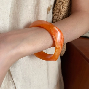 Close-up of orange marble textured acrylic resin bangle worn with linen clothing