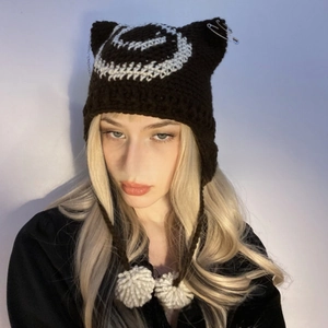 Detail of hand-knitted cat ear hat with white spiral patterns and white pompom ties