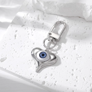 Macro view of silver heart keychain with blue evil eye bead on a textured white stone