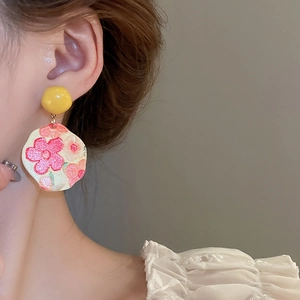 Detail of floral enamel sunflower earrings worn by a model with a soft glazed finish