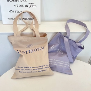 Close-up of beige and lavender canvas tote bags with elegant blue lettering details