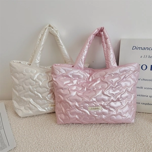 Detail of heart quilted tote bag with pearlescent finish and brand label on beige fabric