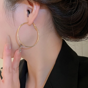 Nahaufnahme eines Models mit großen goldenen Creolen und polierter geometrischer Oberfläche