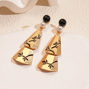 Detail of gold metal earrings with branch engraving and white pearl beads on stone
