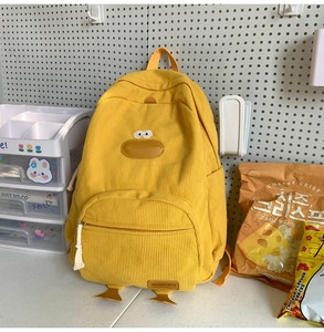 Detail of a yellow corduroy duck backpack on a white pegboard with cute lifestyle props